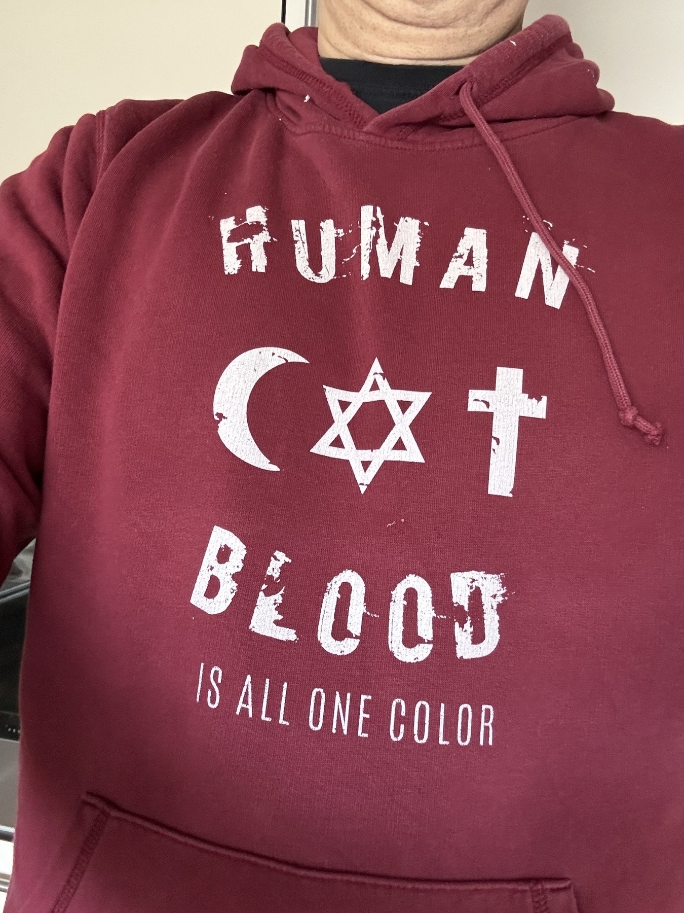 A person is wearing a red hoodie with religious symbols and the phrase "Human blood is all one color."